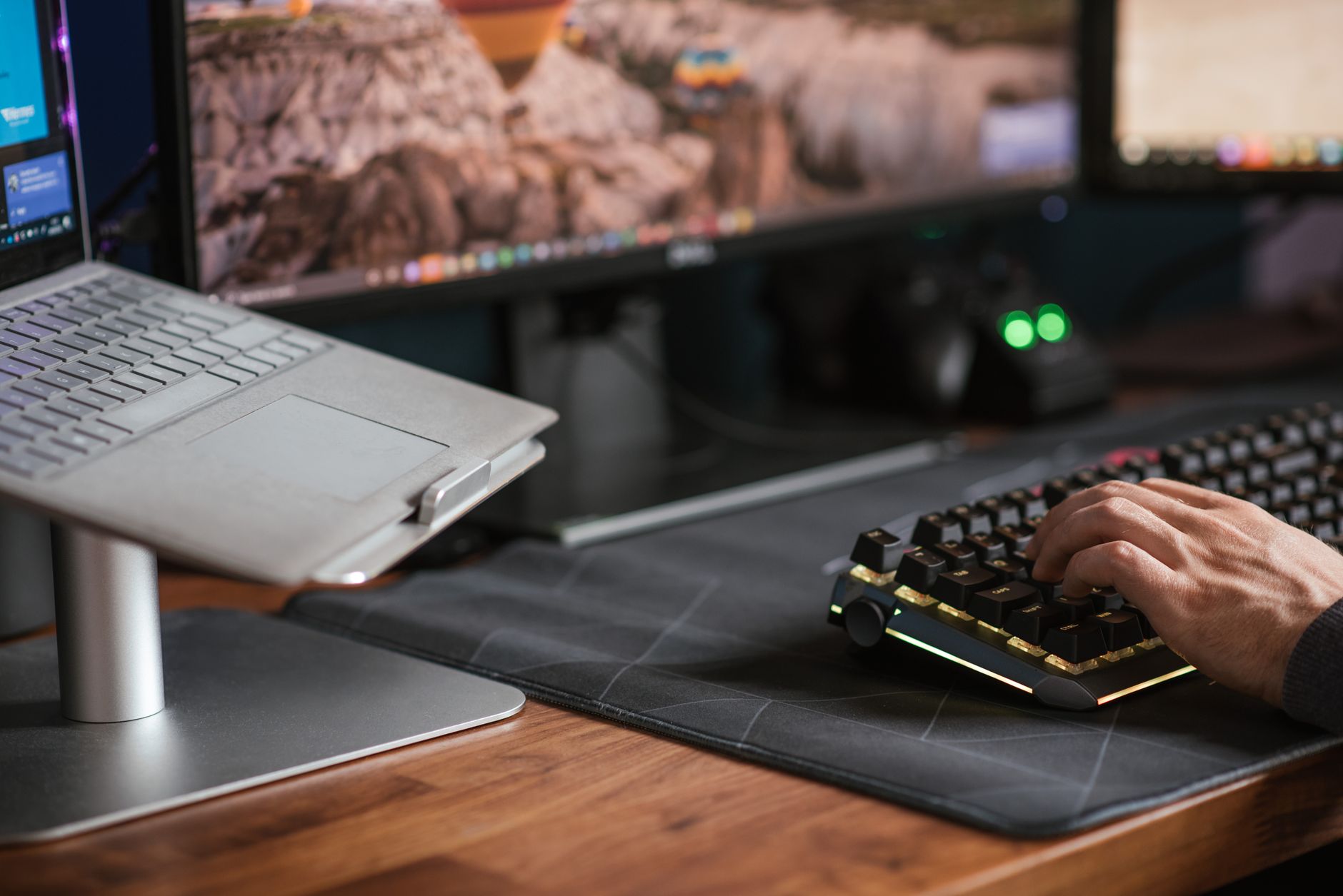Mężczyzna pisze na podświetlanej klawiaturze obok laptopa na podstawce