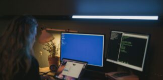 Windows, Linux czy macOS? Porównanie systemów dla programistów i administratorów Kobieta przy kilku monitorach pracująca nad bezpieczeństwem systemów