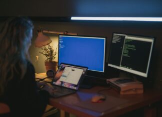 Windows, Linux czy macOS? Porównanie systemów dla programistów i administratorów Kobieta przy kilku monitorach pracująca nad bezpieczeństwem systemów