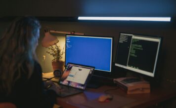 Windows, Linux czy macOS? Porównanie systemów dla programistów i administratorów Kobieta przy kilku monitorach pracująca nad bezpieczeństwem systemów